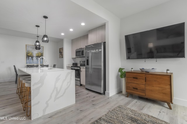 kitchen with stainless steel appliances, a sink, a kitchen breakfast bar, baseboards, and light wood finished floors