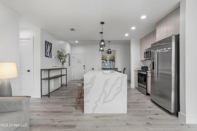 kitchen featuring a breakfast bar area, a sink, visible vents, appliances with stainless steel finishes, and light wood finished floors