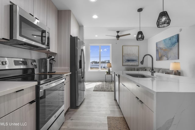 kitchen featuring modern cabinets, appliances with stainless steel finishes, open floor plan, decorative light fixtures, and a sink