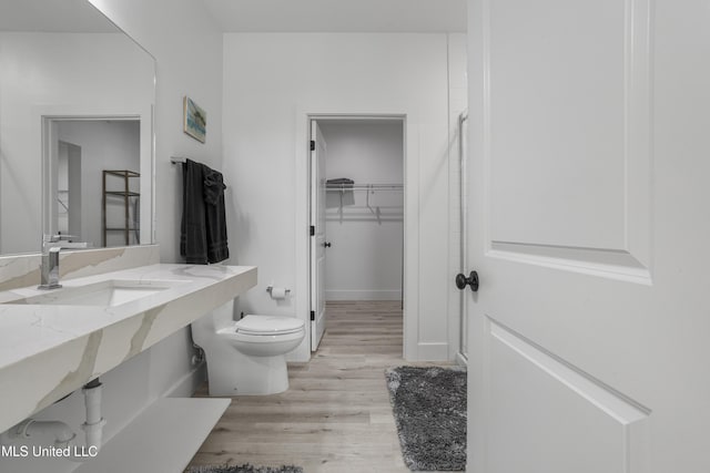 bathroom with baseboards, toilet, wood finished floors, a walk in closet, and a sink