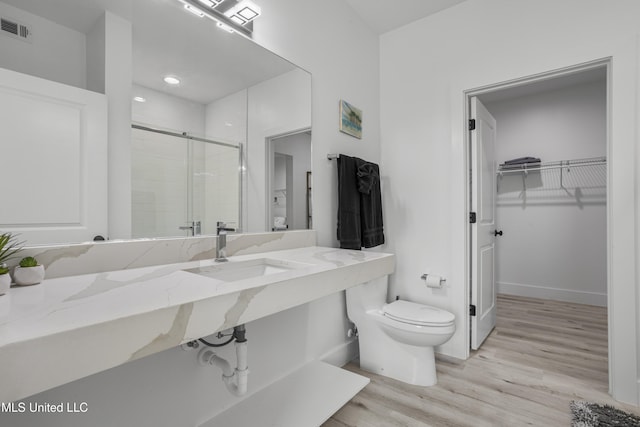 bathroom with toilet, wood finished floors, a sink, visible vents, and a stall shower