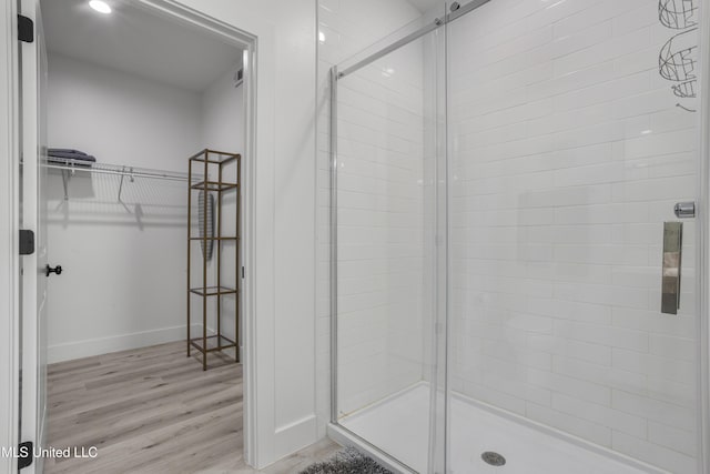 full bathroom featuring wood finished floors, a shower stall, a walk in closet, and baseboards