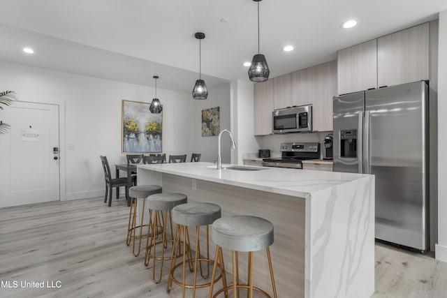 kitchen with an island with sink, appliances with stainless steel finishes, light wood-type flooring, a kitchen bar, and a sink