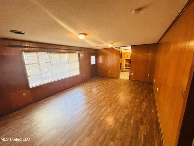 unfurnished living room featuring a textured ceiling, wood-type flooring, a healthy amount of sunlight, and wood walls