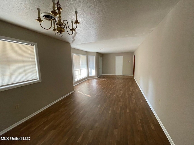 empty room featuring a textured ceiling, an inviting chandelier, and dark hardwood / wood-style flooring