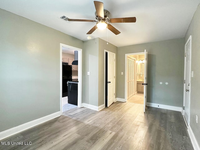 unfurnished bedroom with hardwood / wood-style floors, black fridge, ceiling fan, connected bathroom, and a closet