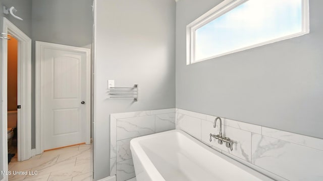 bathroom with marble look tiles and a tub to relax in