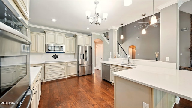 kitchen featuring stainless steel appliances, cream cabinetry, a sink, arched walkways, and a peninsula