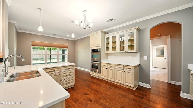 kitchen with a sink, arched walkways, stainless steel double oven, cream cabinetry, and crown molding