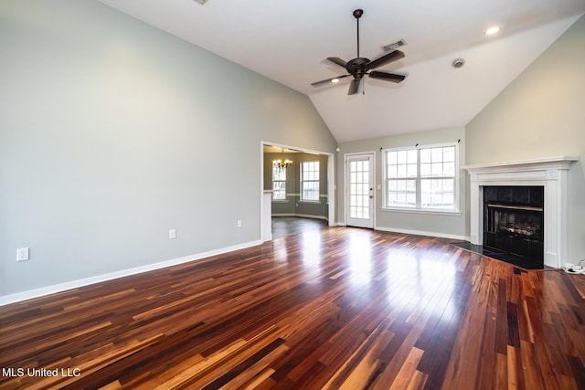 unfurnished living room featuring a tile fireplace, lofted ceiling, dark wood-type flooring, and ceiling fan with notable chandelier