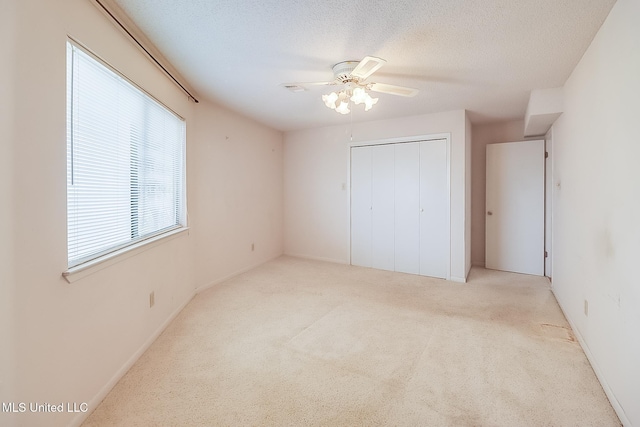 unfurnished bedroom featuring ceiling fan, a closet, light carpet, and a textured ceiling