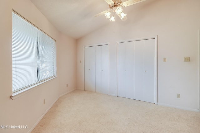 unfurnished bedroom with ceiling fan, light colored carpet, multiple closets, and lofted ceiling