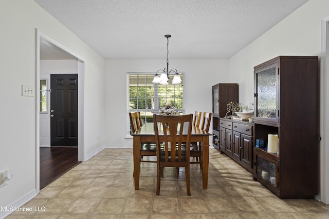 dining space featuring a textured ceiling, a chandelier, and baseboards