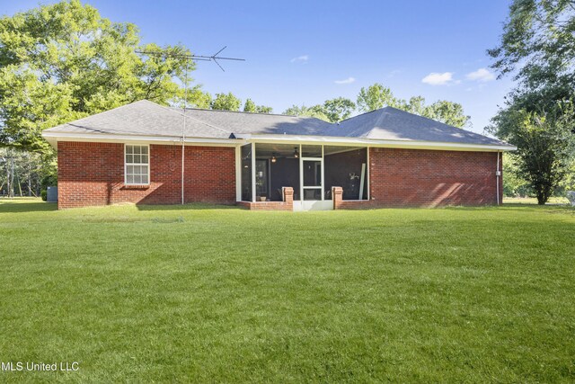rear view of house with a lawn, a sunroom, and brick siding