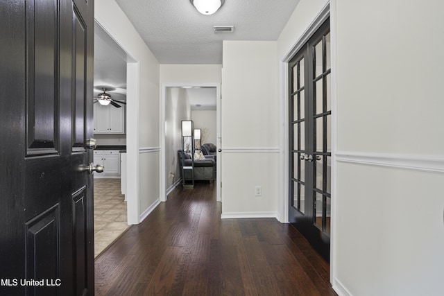 hall with a textured ceiling, baseboards, visible vents, and wood finished floors