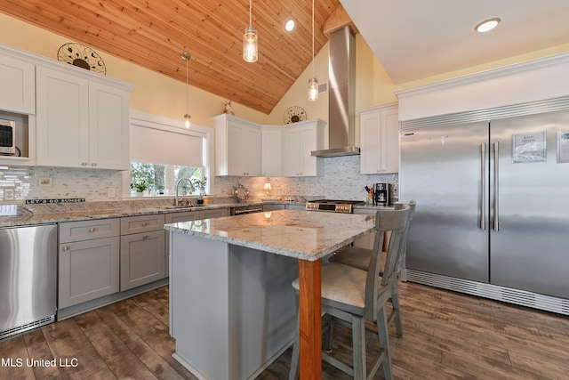 kitchen featuring a center island, stainless steel appliances, wall chimney exhaust hood, pendant lighting, and dark wood-type flooring