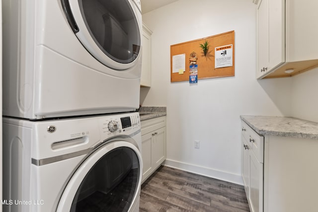 clothes washing area featuring dark hardwood / wood-style flooring, stacked washer / drying machine, and cabinets