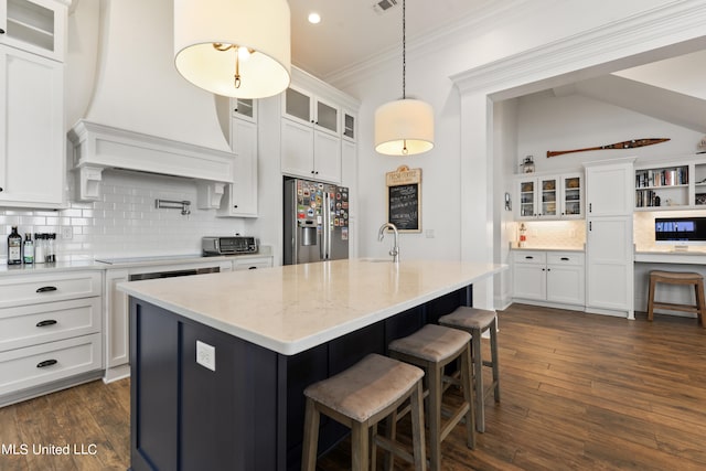 kitchen featuring sink, stainless steel fridge with ice dispenser, custom range hood, a kitchen island with sink, and white cabinets