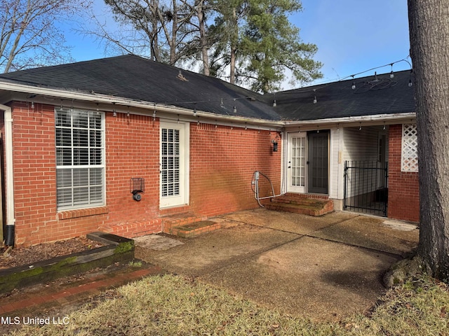 back of property featuring entry steps, roof with shingles, a patio, and brick siding