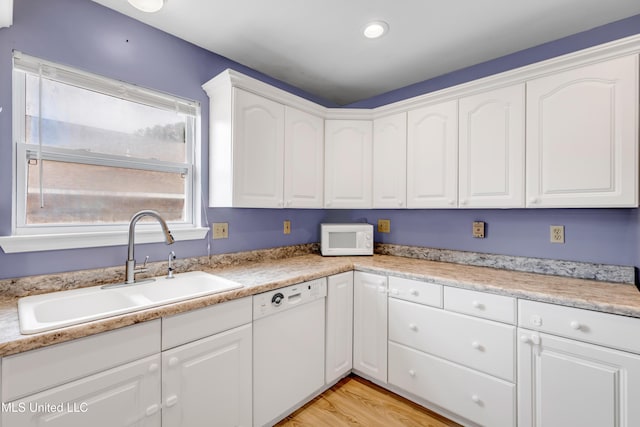 kitchen featuring white appliances, white cabinets, a sink, and light wood-type flooring