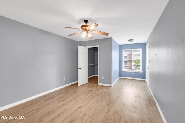 unfurnished bedroom with a closet, wood finished floors, baseboards, a spacious closet, and a ceiling fan