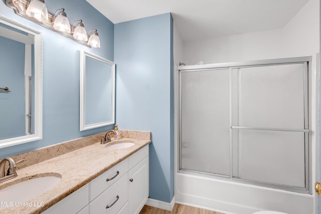 full bath with double vanity, a sink, wood finished floors, and shower / bath combination with glass door