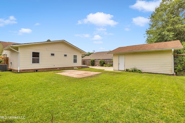 rear view of property featuring fence, central AC, an outbuilding, a patio, and a yard