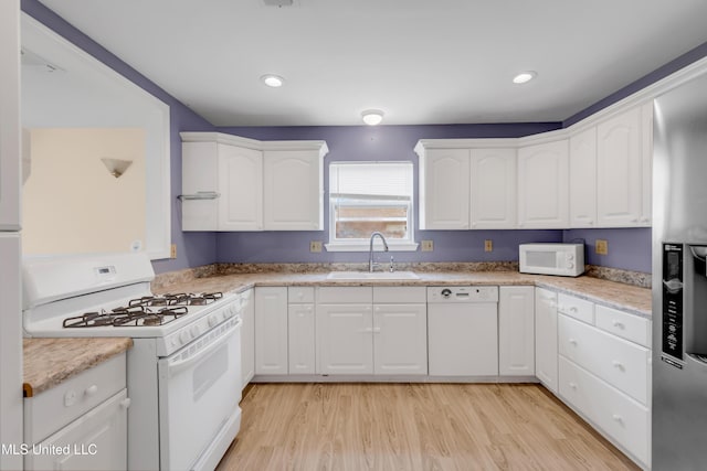 kitchen with a sink, white cabinetry, light wood finished floors, and white appliances