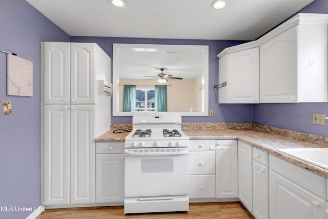 kitchen featuring white cabinets, light countertops, white gas range, a ceiling fan, and light wood-type flooring