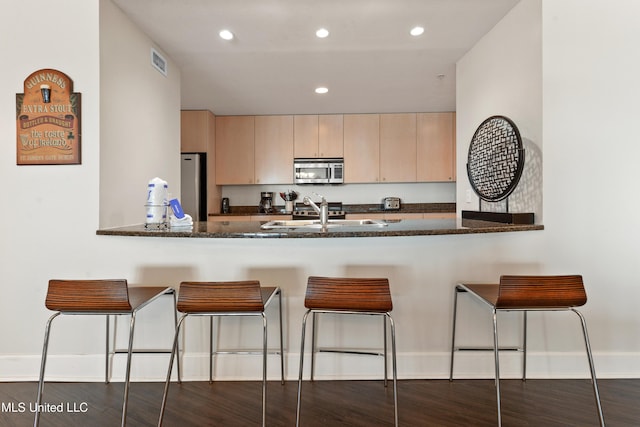 kitchen featuring dark stone countertops, visible vents, a peninsula, light brown cabinetry, and stainless steel appliances