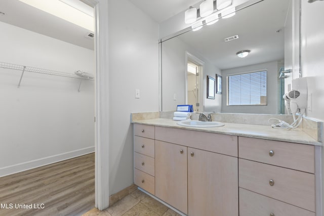 full bathroom with visible vents, a walk in closet, wood finished floors, baseboards, and vanity