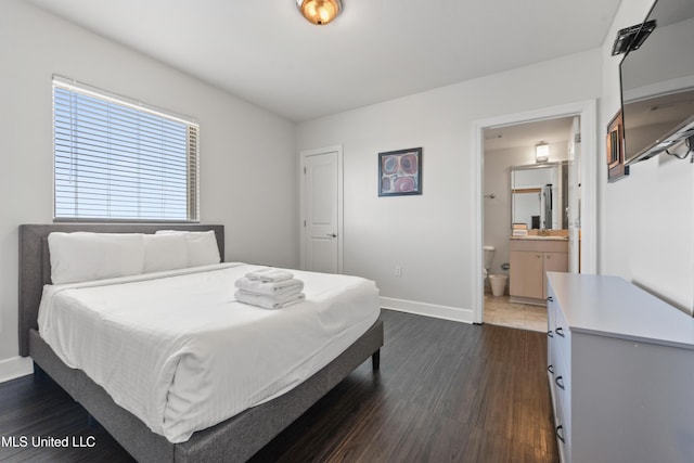 bedroom with dark wood-style floors, ensuite bath, and baseboards