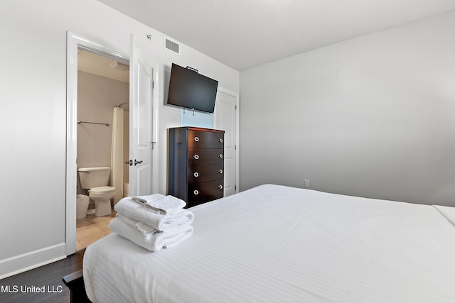 bedroom with ensuite bath, wood finished floors, and visible vents