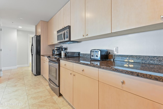 kitchen featuring light brown cabinets, baseboards, dark stone counters, light tile patterned flooring, and appliances with stainless steel finishes