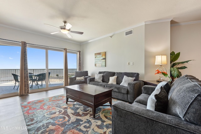 living area featuring ceiling fan, wood finished floors, visible vents, and ornamental molding