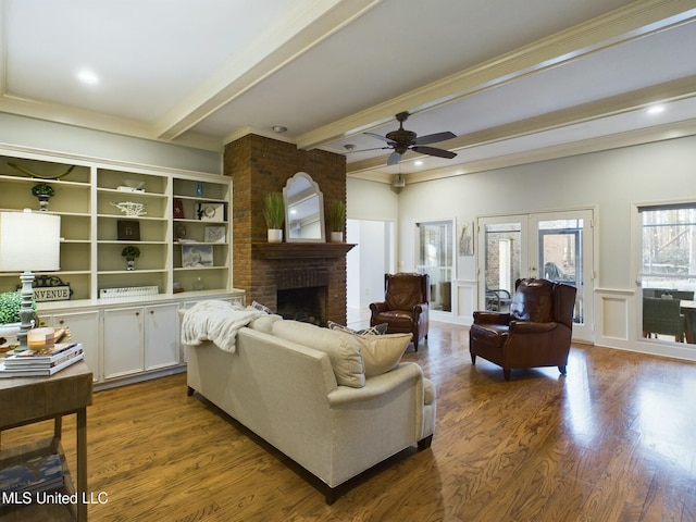 living room featuring hardwood / wood-style floors, beamed ceiling, ceiling fan, a brick fireplace, and crown molding