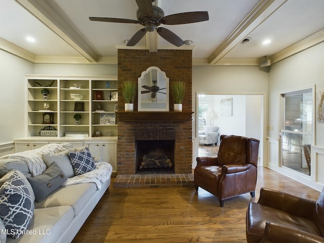 living room featuring ceiling fan, beam ceiling, wood-type flooring, and a brick fireplace