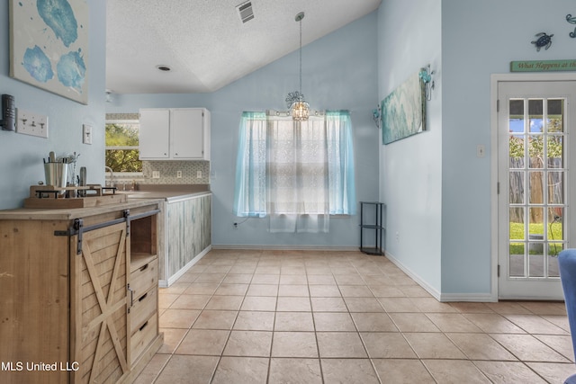 172 Briarfield Ave, Biloxi, MS 39531 - kitchen featuring light tile patterned floors, white cabinetry, lofted ceiling, a textured ceiling, and healthy amount of natural light