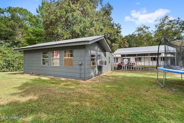 back of house with a trampoline, a lawn, and a carport