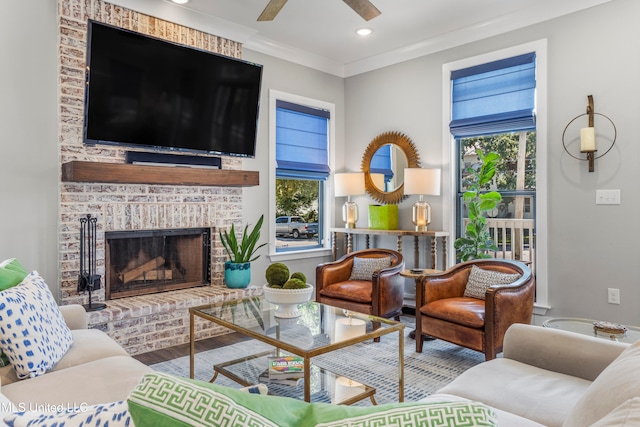 living room featuring wood-type flooring, a brick fireplace, ceiling fan, and crown molding