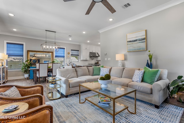 living room featuring ceiling fan with notable chandelier, light wood-type flooring, and crown molding