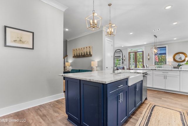 kitchen with light stone counters, light wood-type flooring, an island with sink, and hanging light fixtures