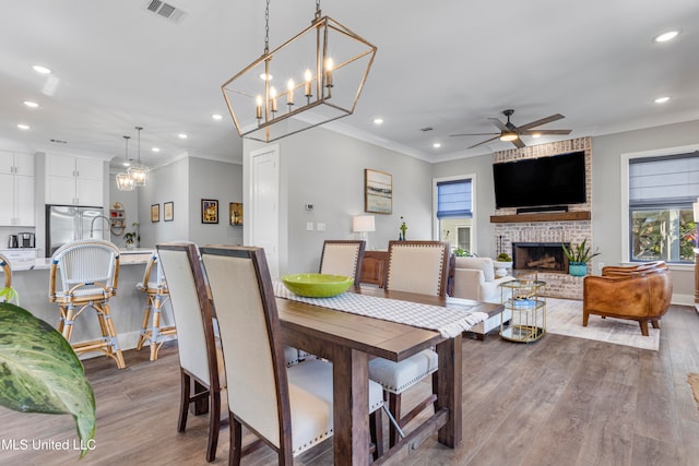 dining room featuring ceiling fan with notable chandelier, light wood-type flooring, a fireplace, and ornamental molding