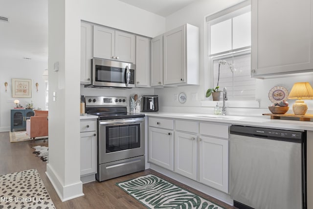 kitchen featuring appliances with stainless steel finishes, light countertops, a sink, and dark wood-style floors