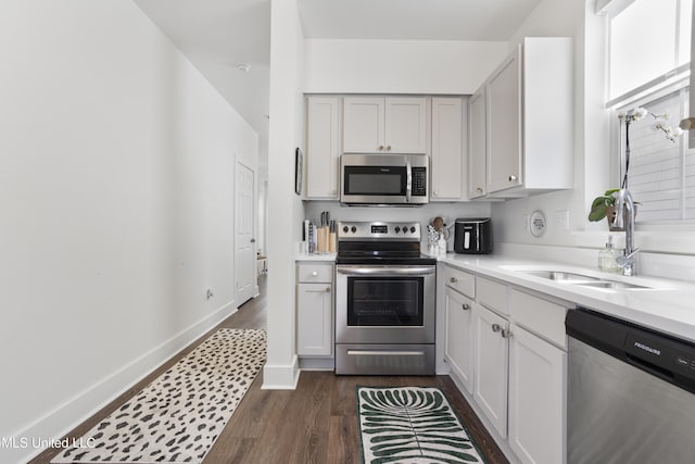 kitchen with dark wood-style floors, stainless steel appliances, light countertops, a sink, and baseboards