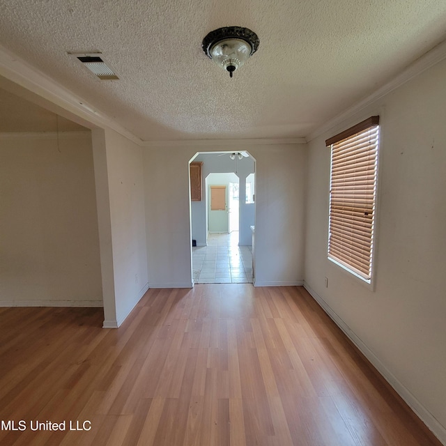 unfurnished room featuring light wood finished floors, a textured ceiling, visible vents, and arched walkways