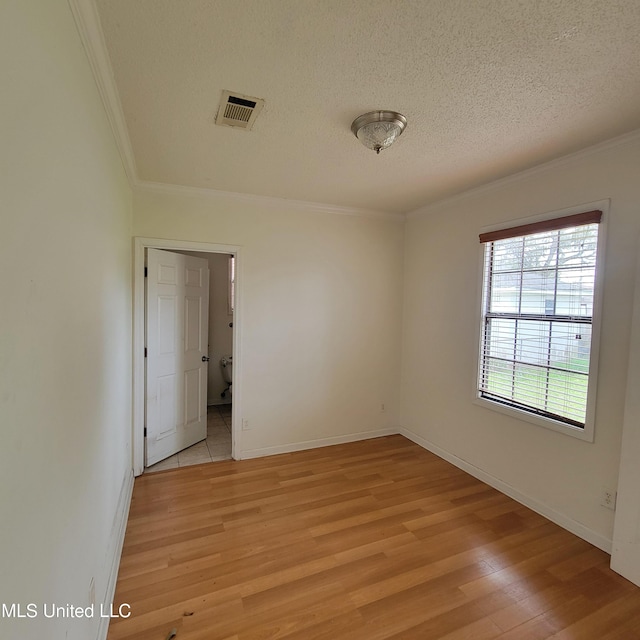 spare room featuring light wood finished floors, crown molding, a textured ceiling, and visible vents