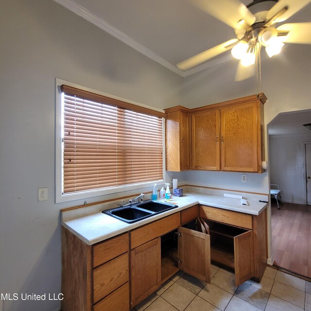 kitchen featuring a sink, brown cabinets, crown molding, ceiling fan, and light countertops