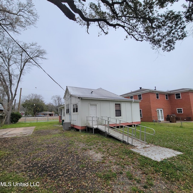 rear view of house featuring a lawn, board and batten siding, fence, metal roof, and central AC unit