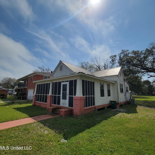 view of home's exterior featuring a sunroom, fence, metal roof, a lawn, and central AC unit